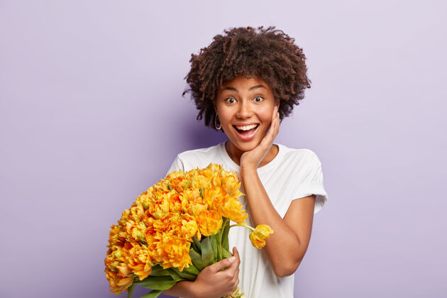 快乐快乐的女性 牙齿般的微笑 清爽的头发 快乐的接受男友的求婚 捧着一束漂亮的黄花 隔离在紫色的墙壁上积极的情绪和情感概念姿势爽朗反应