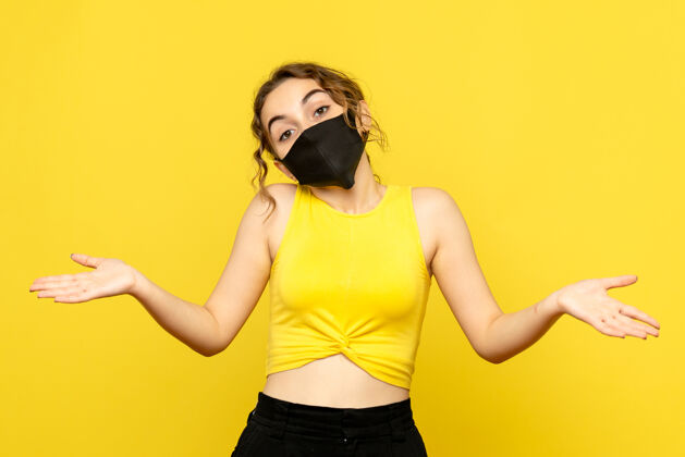 女性黄墙上戴着黑面具的年轻女子的正视图成人面具病毒