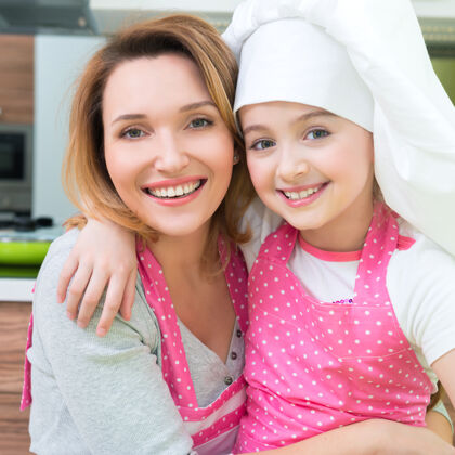 妈妈厨房里穿着粉色围裙的快乐微笑的母女画像女食物围裙