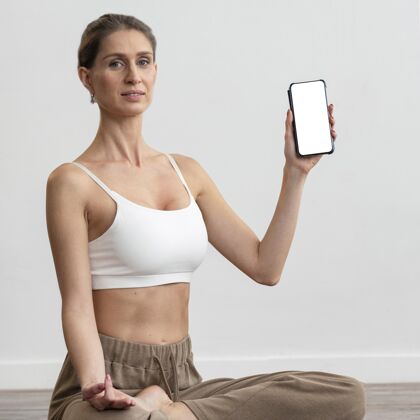 复制女人在家做瑜伽 拿着智能手机锻炼放松冥想