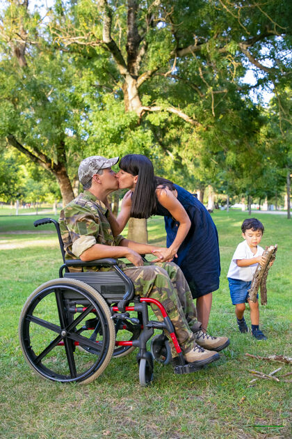 退休穿军装的残疾人一边亲吻妻子 一边在公园里扛柴火残疾退伍军人或家庭户外概念野餐柴火退伍军人