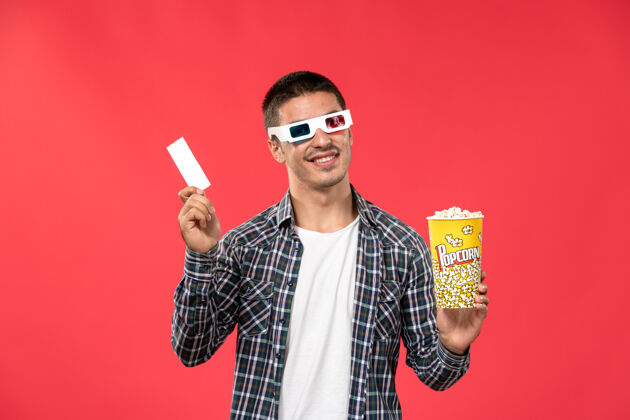 男性正面图年轻男子手持爆米花包和票上的浅红墙电影院电影男电影票电影院