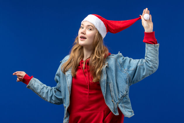 情感正面图：戴着红色圣诞帽的年轻女性 蓝色背景 带着圣诞色彩年轻观点帽子