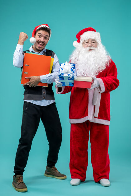 圣诞快乐圣诞老人与年轻人和礼物在蓝色墙上的正面视图假期男性圣诞