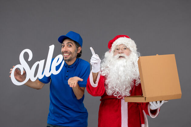 服装圣诞老人的正面图 男性信使手持销售横幅 灰色墙上有食品盒庆祝男圣诞老人