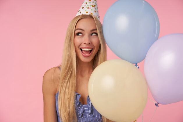 空气一位年轻快乐的金发女子站在粉红色的背景下 在五彩的气球里摆姿势 庆祝节日 和朋友们一起欢庆美好的聚会发型帽子圆锥形