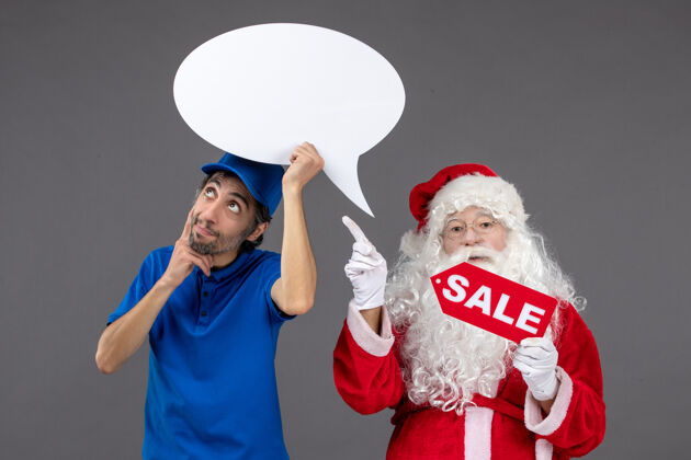 快乐圣诞老人的正面图 灰色墙上的男性信使手持白色标牌和销售横幅前面销售工作