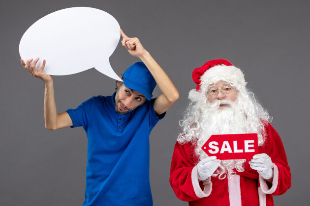 举行圣诞老人与男信使手持白色标志和灰色墙上的销售横幅的正面视图人服装快递