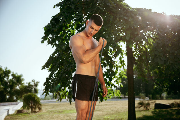人一位肌肉发达的男运动员在公园里锻炼身体体操 训练 健身 柔韧性锻炼夏日城市阳光明媚 生活方式积极健康 青春活力 健美肌肉成人运动
