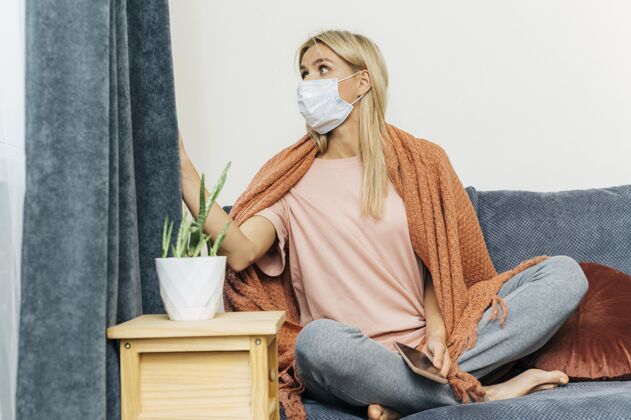 预防大流行期间 家里戴着医用口罩 透过窗帘看外面的女人医学面具冠状病毒面具