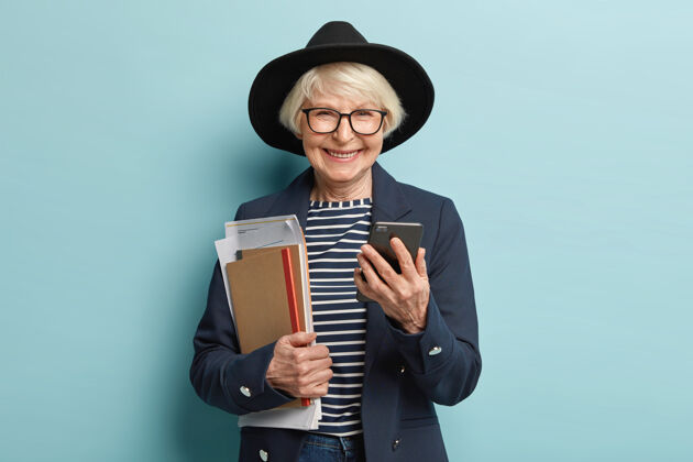肖像成功的上了年纪的面带微笑的女商人在手机上查看数据信息 拿着带文件的记事本 从重要会议回来 穿着时髦的衣服 在网上付款乐观手机经理