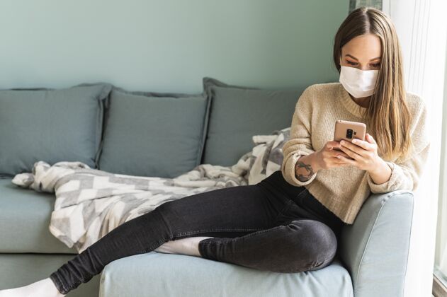 预防大流行期间 戴着医用口罩的妇女在家里用智能手机隐居隔离病毒