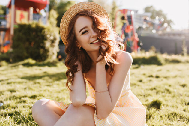 户外穿着黄色裙子的姜黄色女孩在草地上摆姿势戴着帽子的浪漫女士坐在绿色草坪上大笑可爱阳光姜