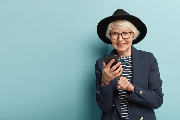 电话资深快乐女士戴着光学眼镜在手机上做网上银行 使用现代科技在互联网上搜索信息 穿着时尚服饰 微笑友好 与世隔绝皱纹外表女士
