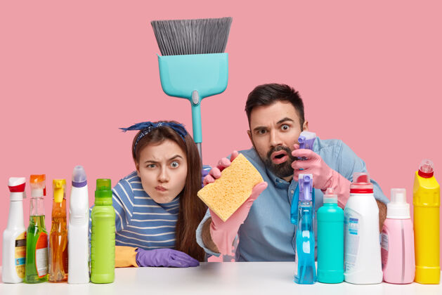清洁镜头中的女人和男人一丝不苟地看着 做家务 打扫一切 拿着海绵和扫帚 坐在工作场所用洗涤剂 隔着粉红色的墙壁家务Omg团队合作室内