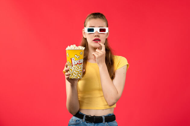 戏剧正面图年轻女性在电影院拿着爆米花 带着思考的表情在红墙电影院小吃女性趣味电影女性小吃电影