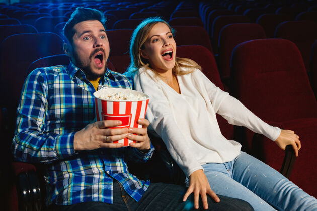 电影迷人的年轻白种人夫妇在电影院 房子或电影院看电影看起来富于表现力 惊讶和情绪化独自坐着玩关系 爱情 家庭 周末时间娱乐夫妇女人