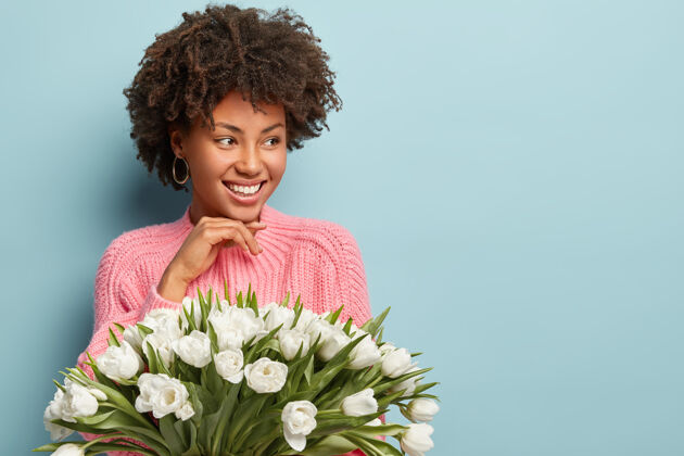 欢乐时间 好心情和种族观念快乐的美国黑人女人 卷发 面带微笑 手持白色芳香的花朵 隔着蓝色的墙壁 空白处旁边女人个人