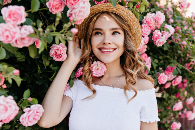 树可爱的蓝眼睛女孩戴着夏天的帽子在花园里摆姿势快乐的卷发女人拿着玫瑰笑的户外肖像明亮公园表情