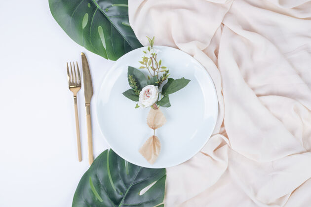 盘子一朵玫瑰放在白色的盘子里 上面有假叶子和桌布绿婚礼植物