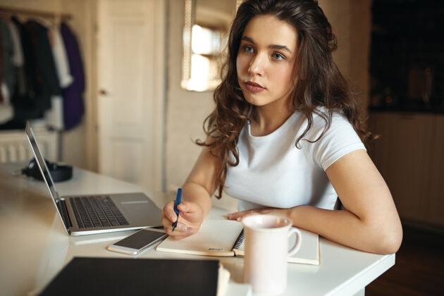 课程沉思沉思的女学生在家里学习 坐在办公桌前打开笔记本电脑的画像作家学习设备