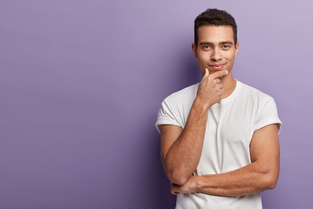 肖像帅哥的半身镜头托着下巴 直接用满意自信的表情看着 穿着白色t恤 在紫色的墙上摆姿势 腾出空间干净个性肌肉