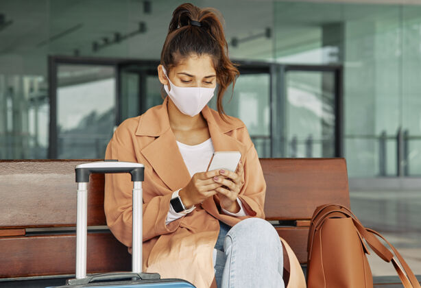 Covid19大流行期间 一名戴着医用口罩的妇女在机场使用智能手机病毒水平医疗