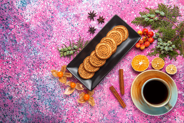 美味俯视图中的甜饼干内的黑色形式与茶和肉桂杯浅粉红色的表面食物里面形状
