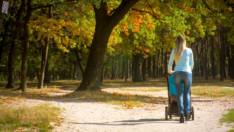 自然秋日公园 年轻女子带着婴儿车行走的后景秋天公园婴儿车乐趣