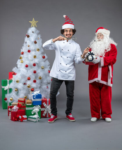 圣诞快乐圣诞老人和男厨师在灰色墙上围着圣诞礼物的正视图礼物十二月快乐