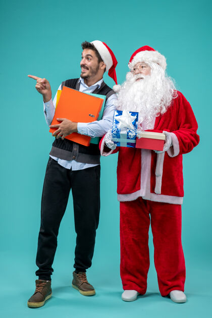 圣诞圣诞老人与年轻男性和礼物在蓝色墙上的正面视图假期男性圣诞快乐