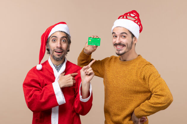 男人前视图两个圣诞男人一个穿着圣诞老人外套 另一个手放在米色隔离背景的腰部风景圣诞节男人