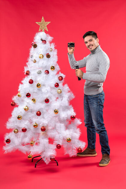 拿着圣诞气氛严肃的年轻人站在装饰好的圣诞树旁拿着麦克风拍照站着庆祝装饰