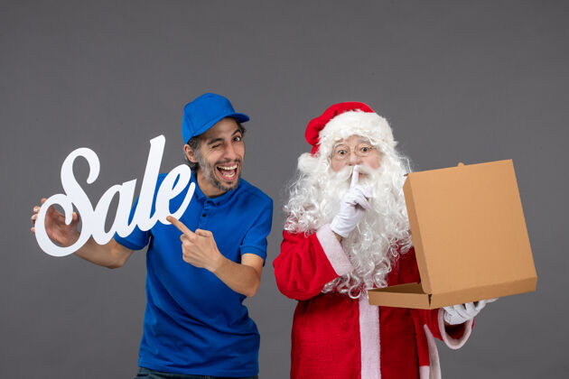 快乐圣诞老人的正面图 男信使拿着卖东西的字条和灰墙上的食品盒快递庆祝快乐