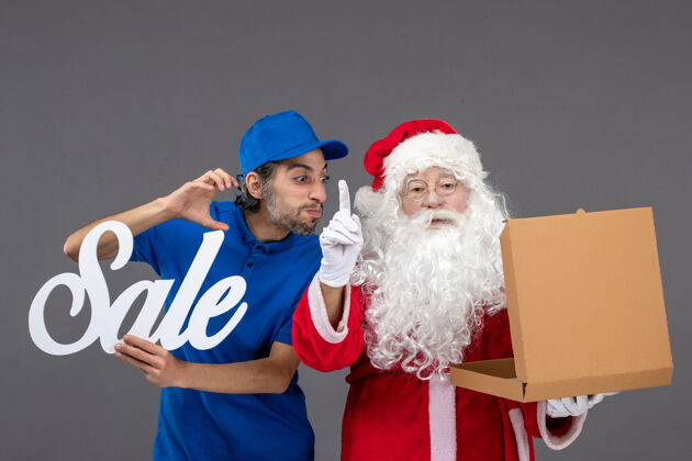 写作圣诞老人的正面图 男信使拿着卖东西的字条 灰色墙上挂着空的食品盒人圣诞老人圣诞老人