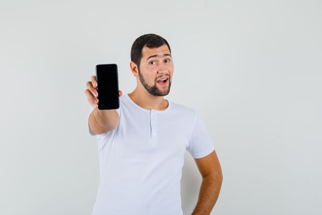男人身穿白色t恤的年轻人展示着手机 看上去很开心 前视图人帅哥成人