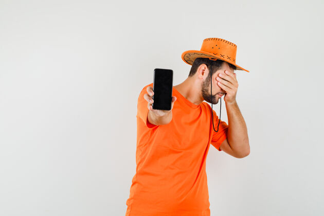 休闲年轻人展示着手机 穿着橙色t恤 戴着帽子 看上去很害怕帽子男性成人