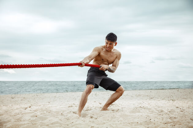 年轻年轻健康的男子运动员在海滩上做深蹲海滩锻炼训练