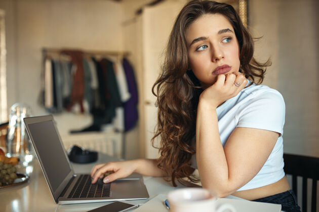 工作场所侧视图美丽的年轻女性自由职业者与蓝色的眼睛有无聊悲伤的表情坐在她的笔记本电脑工作场所互联网专业企业家