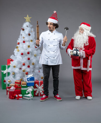 礼物圣诞老人和男厨师在灰色墙上围着圣诞礼物的正视图可爱十二月节日