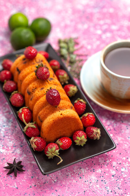 茶顶视图美味的烤蛋糕在黑色蛋糕锅里 新鲜的红色草莓茶和柠檬放在粉红色的桌子上新鲜食物糖