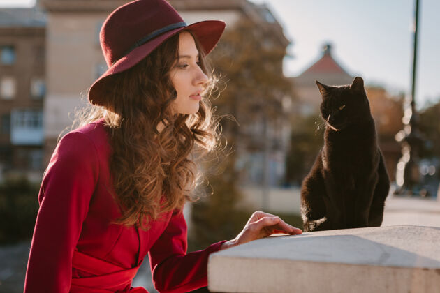 女人美丽时尚的女人穿着紫色西装在城市街头 春夏秋冬时节时尚潮流戴着帽子 看着一只猫优雅女士深色