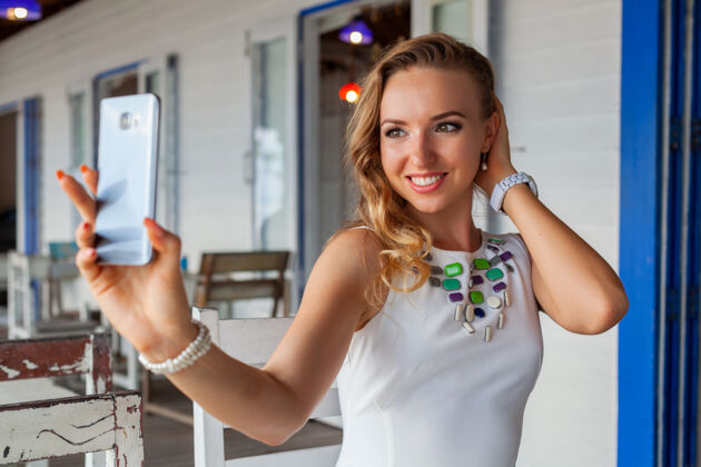 漂亮一位身着白色礼服的美女戴着墨镜在夏日咖啡馆用手机拍照女孩衣服户外