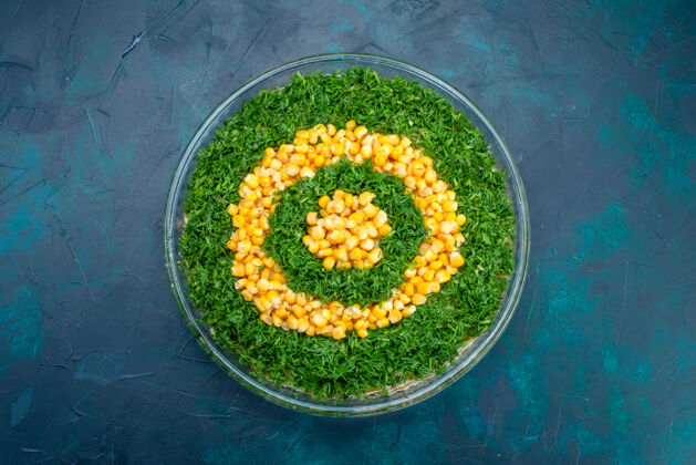 蔬菜顶视图：深蓝色背景的圆形玻璃盘内有玉米的绿色沙拉玻璃杯健康的圆的