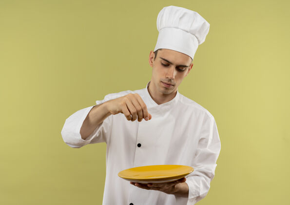 男年轻的男厨师穿着厨师制服 看起来像盘子里撒盐的样子制服厨师盘子