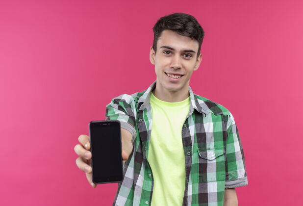 粉色微笑的白人年轻人穿着绿色衬衫 在孤立的粉色背景下对着镜头拿着手机穿着微笑小伙子
