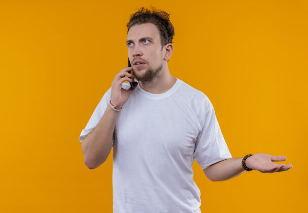 电话看着身边穿着白色t恤的年轻人在电话里说话 手拉着手站在孤立的橙色背景上手穿年轻