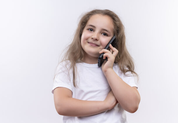 女孩微笑的小女孩穿着白色t恤在孤立的白色背景下讲电话小穿着微笑