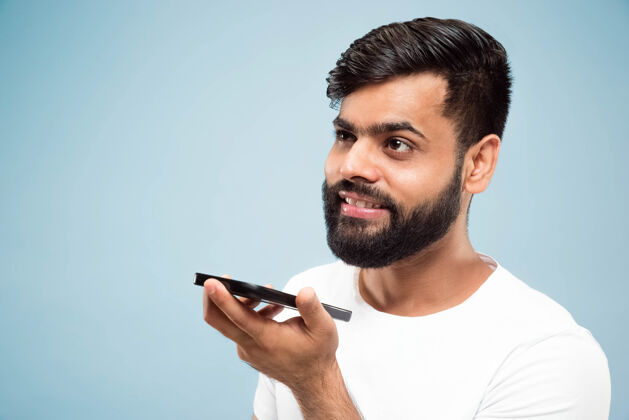 男性蓝色背景上穿着白衬衫的印度教年轻人的半身特写肖像人类情感 面部表情 广告概念负面空间打电话 录音留言看呼叫工作