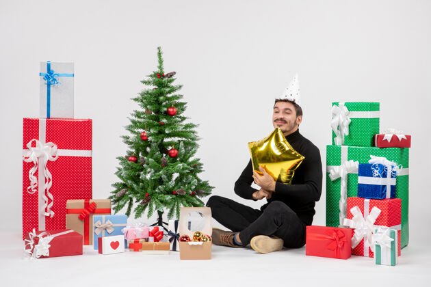 圣诞节年轻人围坐在礼物旁边 拿着金星在白墙上情感礼物节日